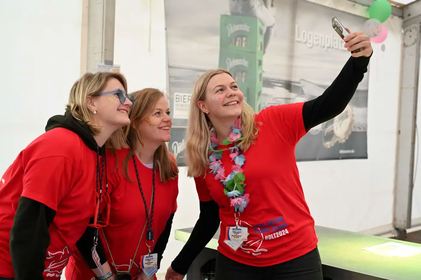 Eine Gruppe lächelnder Menschen, die sich in einer entspannten Atmosphäre vergnügen. Sie tragen grüne T-Shirts und scheinen Spaß bei einem Event zu haben. Di...