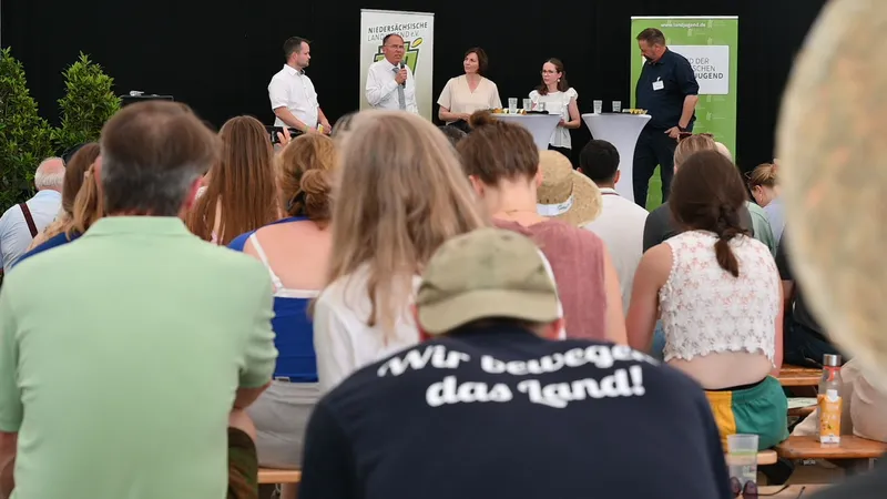 Viele junge Menschen von hinten. Wir bewegen das Land, steht auf einem der T-Shirts. Alle schauen auf eine Bühne, auf der Bundespolitik und BDL talkt.