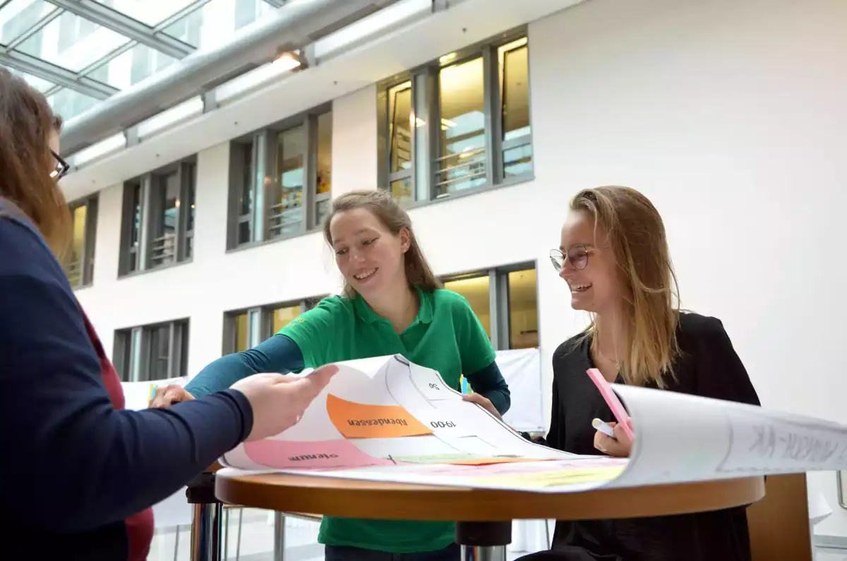 Drei junge Frauen in Anzügen sitzen an einem Tisch und diskutieren bei einem Workshop zur Jugendpolitik. Sie lächeln und scheinen sich wohlzufühlen. 
