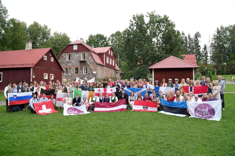 Junge Menschen aus Europa, viele mit Landesflaggen, nehmen an einer European Rally in Estland teil. Sie stehen vor einem Hintergrund aus Himmel, Bäumen und e...
