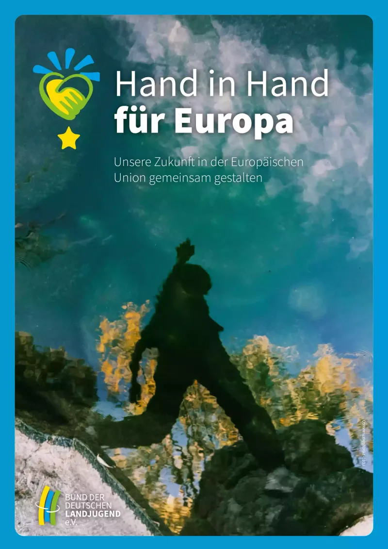 Ein Poster mit dem Titel "Hand in Hand für Europa", das zwei Hände zeigt, die sich über einem Globus halten. Der Hintergrund zeigt eine natürliche Landschaft.