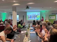 Junge Leute in einem Raum lachen über ein Foto, dass auf der Bühne gezeigt wird