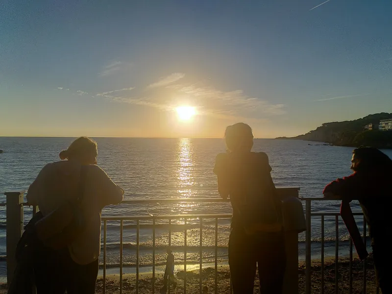 Janina Sarsky steht am Rande eines Sees und blickt auf den Sonnenuntergang. Das Wasser spiegelt die letzten Sonnenstrahlen und der Himmel erstrahlt in warmen...