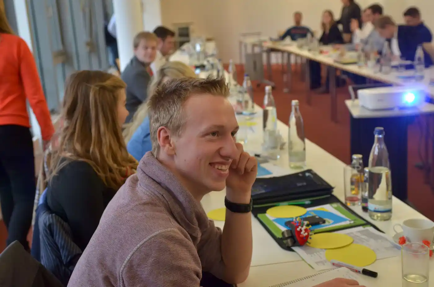 Junges Team bei einem BDL-Arbeitskreis. Sie sitzen an einem Tisch mit Getränken und diskutieren angeregt. Ein Lächeln auf den Gesichtern zeigt ihre positive ...