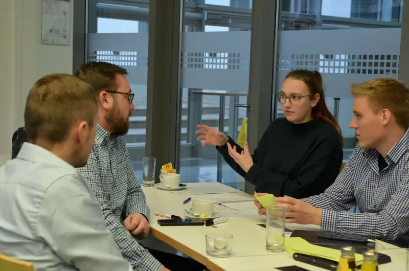 Junge Landwirte und Landwirtinnen diskutieren auf einem Hof über Agrarpolitik. Sie sitzen an einem Tisch und tauschen Gedanken aus. Der Tisch ist mit Unterla...