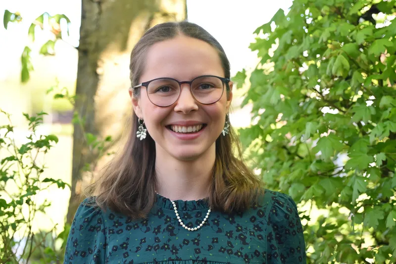 Porträt einer jungen Frau vor einem landschaftlichen Hintergrund.