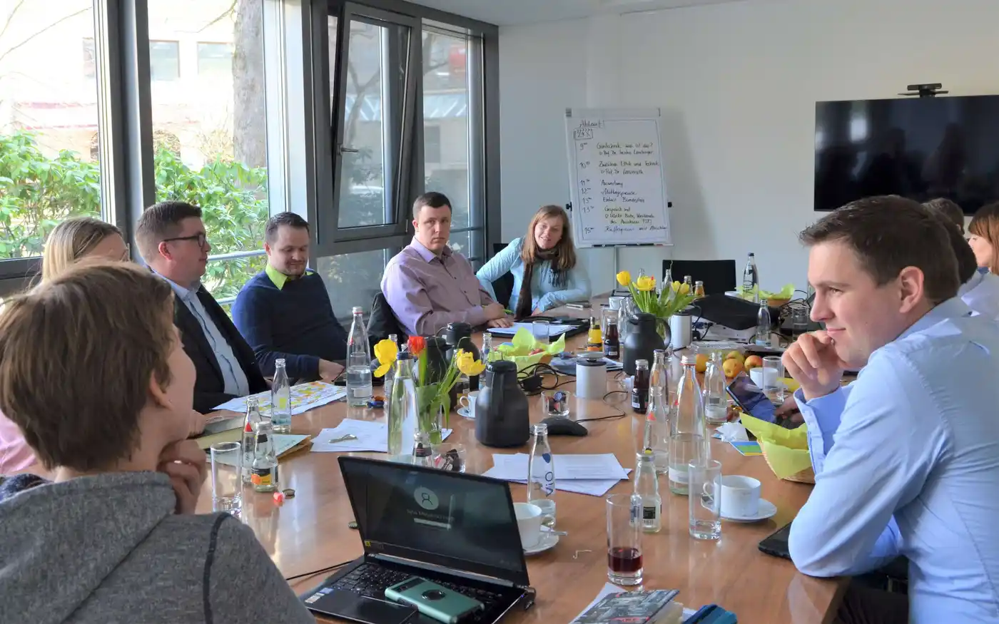 Ein Team von Ingenieuren arbeitet gemeinsam an einem Projekt an einem Tisch. Auf dem Tisch stehen Laptop, Getränke, Teller und Pflanzen. Es wird ein gesellig...