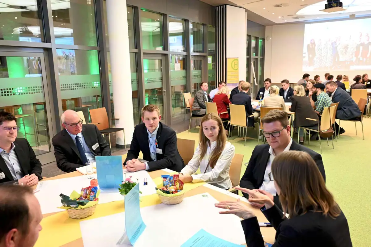 Ein großer Raum mit Personen an großen Gruppentischen