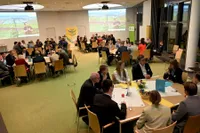 Ein großer Raum mit Personen an großen Gruppentischen