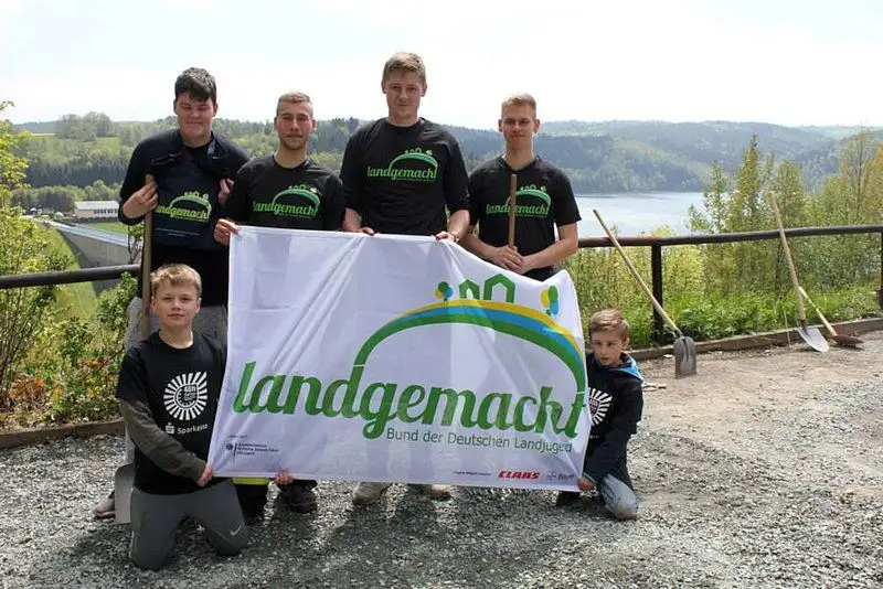 Zwei lächelnde Jugendliche in T-Shirts und Shorts genießen die Natur. Sie stehen unter einem blauen Himmel mit Wolken vor einem Baum und einem grünen Strauch...