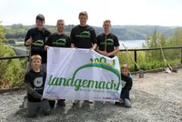 Zwei lächelnde Jugendliche in T-Shirts und Shorts genießen die Natur. Sie stehen unter einem blauen Himmel mit Wolken vor einem Baum und einem grünen Strauch...