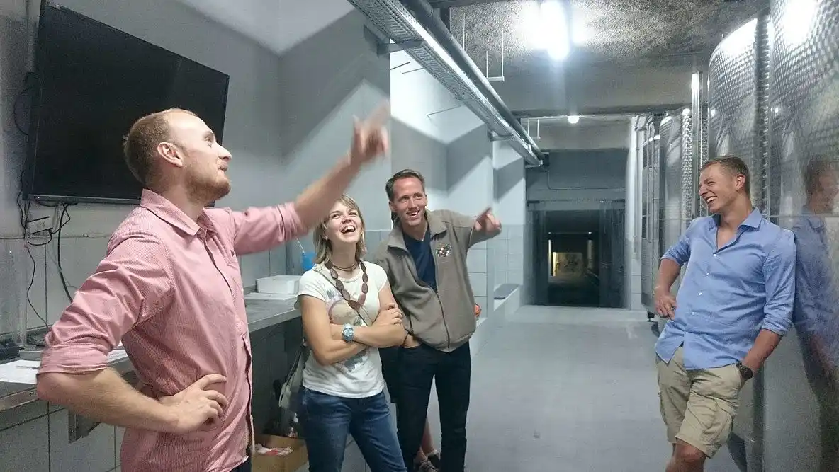 Ein Ingenieur lächelt bei einem Event, während er mit erhobenem Arm und gespreizten Fingern eine Geste macht. Er steht entspannt und trägt ein T-Shirt. Der M...