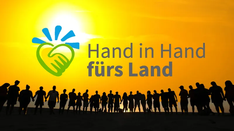 Ein Team von glücklichen Menschen lächelt in die Kamera, während sie in der Natur stehen. Sie halten ein Banner mit dem Logo der HiH und einem Schriftzug in ...