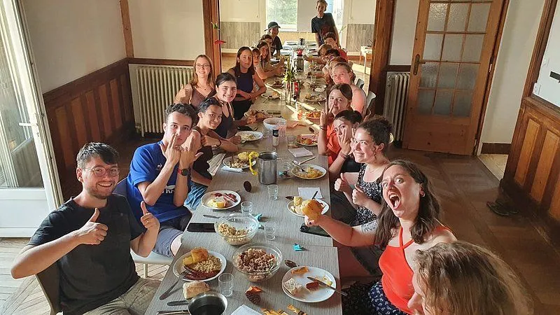 Freunde genießen ein gemeinsames Essen am Tisch. Auf dem Tisch stehen Teller mit leckerem Essen, Besteck und Getränken. Die Menschen lächeln und scheinen Spa...