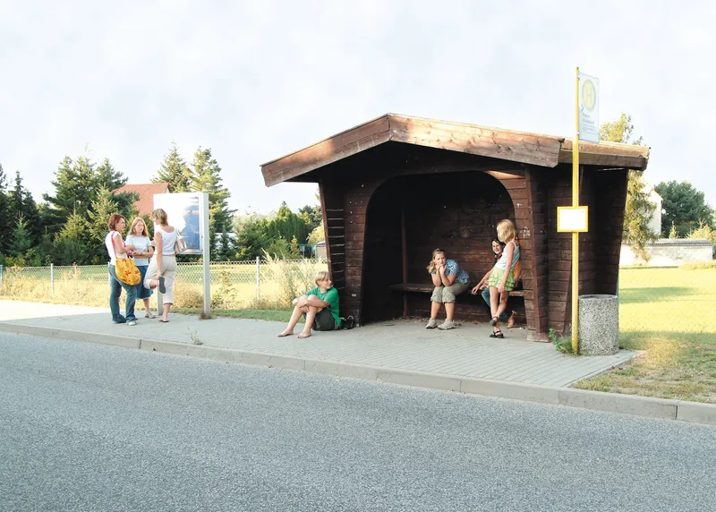 Junge Menschen treffen sich an einer Bushaltestelle, einem Holzhäuschen.